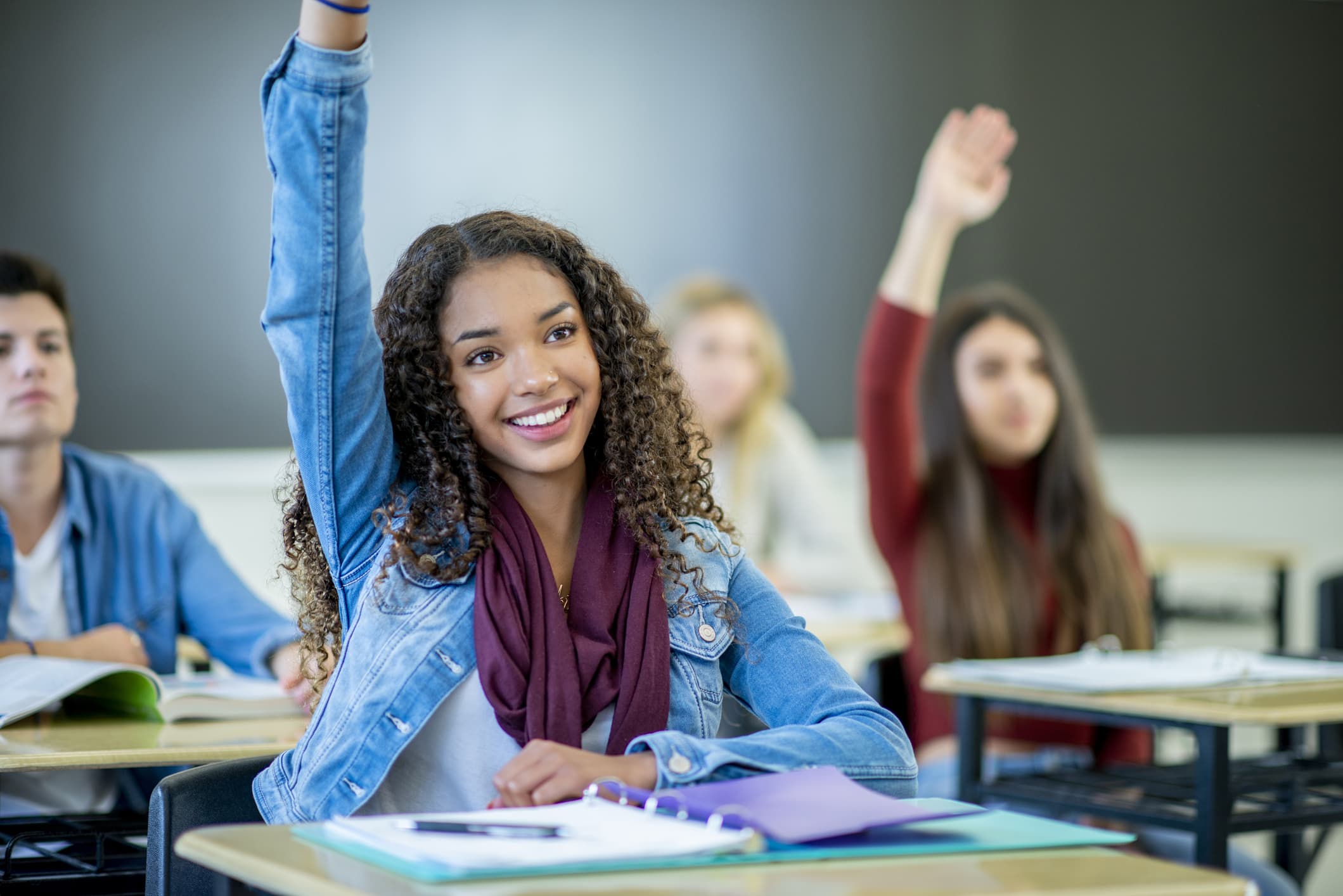 Student raising her hand in a classroom learning